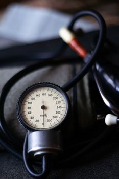 Analog tonometer with cuff and phonendoscope on old suitcase. Close up view and blurred background. Underexposed photo.