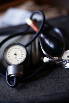 Analog tonometer with cuff and phonendoscope on old suitcase. Close up view and blurred background. Underexposed photo.