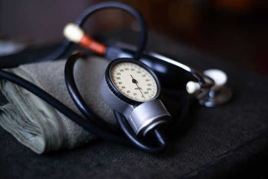 Analog tonometer with cuff and phonendoscope on old suitcase. Close up view and blurred background. Underexposed photo.