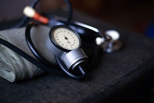 Analog tonometer with cuff and phonendoscope on old suitcase. Close up view and blurred background. Underexposed photo.