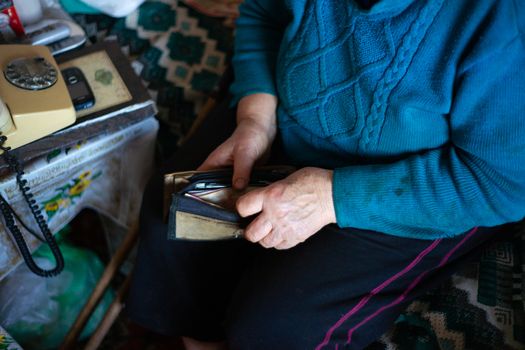 Old poor gray hair woman holds Ukrainian hryvna money in her hands. Woman is sad. Poor life in village. Old age not good. Low-light photo.