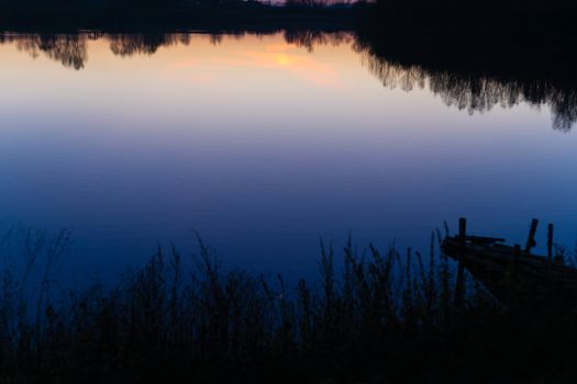 Blue time evening sky landscape with trees and lake in foreground. Blue time sunset. Perfect teal and orange colors. Low-light underexposed photo.