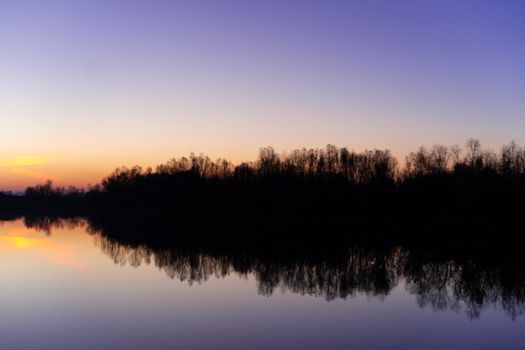 Blue time evening sky landscape with trees and lake in foreground. Blue time sunset. Perfect teal and orange colors. Low-light underexposed photo.