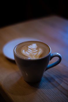 A low light shot of cappuccino cup with latte art on wooden table.