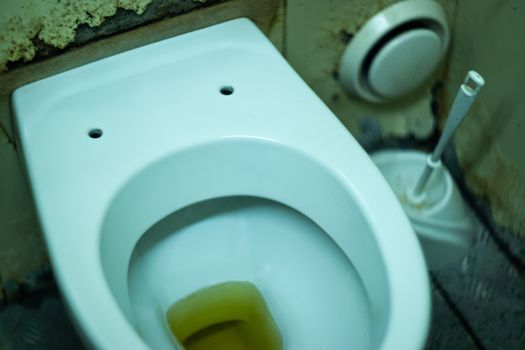 Dirty terrible toilet in a public toilet. Plating deteriorated from moisture and urine. Hue yellow urine in toilet, dirty floor.