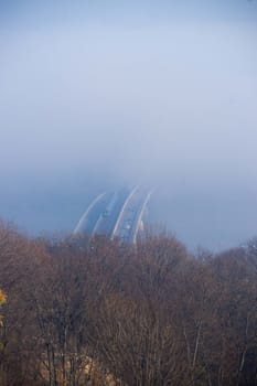 Autumn fog and river steel bridge with subway train on blurred background. Forest in foreground.