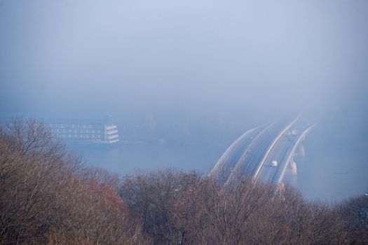 Autumn fog and river steel bridge with subway train on blurred background. Big floating boat hotel in river. Forest in foreground.