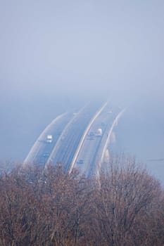 Autumn fog and river steel bridge with subway train on blurred background. Forest in foreground.