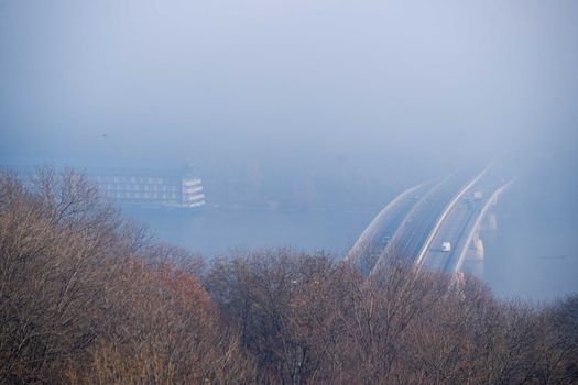 Autumn fog and river steel bridge with subway train on blurred background. Big floating boat hotel in river. Forest in foreground.