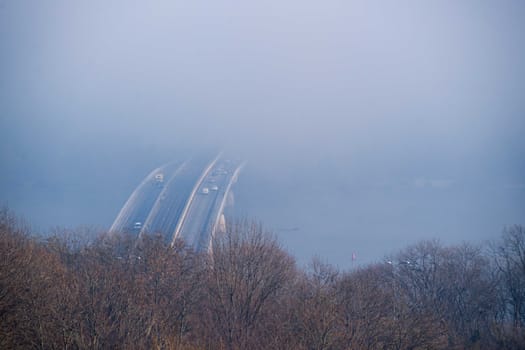 Autumn fog and river steel bridge with subway train on blurred background. Forest in foreground.