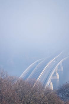 Autumn fog and river steel bridge with subway train on blurred background. Forest in foreground.