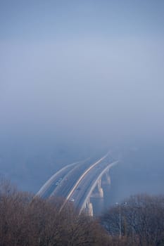 Autumn fog and river steel bridge with subway train on blurred background. Forest in foreground.