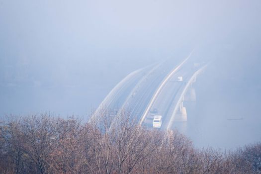 Autumn fog and river steel bridge with subway train on blurred background. Big floating boat hotel in river. Forest in foreground.