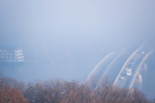 Autumn fog and river steel bridge with subway train on blurred background. Big floating boat hotel in river. Forest in foreground.