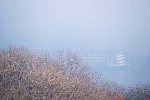 Autumn fog and big floating hotel in river on blurred background. Forest in foreground.