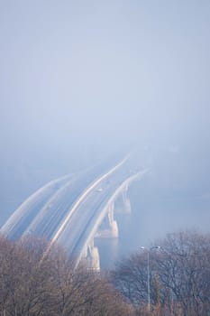 Autumn fog and river steel bridge with subway train on blurred background. Forest in foreground.