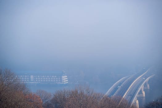 Autumn fog and river steel bridge with subway train on blurred background. Big floating boat hotel in river. Forest in foreground.
