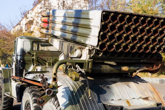 Camouflage military truck with rocket launcher. Outdoor military vehicles museum. Armor is damaged at the battlefield. Missile firing system on military armored truck close up view. Rocket launcher.