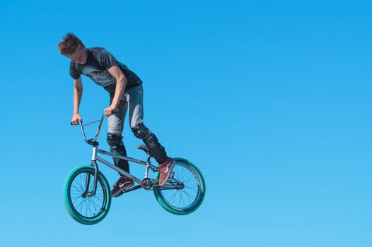 Young BMX biker with leg protect on BMX doing air trick on background sky
