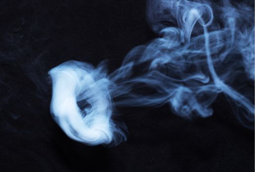 White smoke ring on black fabric background. Smoke spreads over the background. Vaping culture, life without cigarettes. Conceptual image.