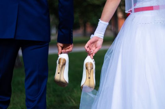 The bride and groom hold the shoes of the bride between themselves and hold hands with their little fingers. Wedding in detail.