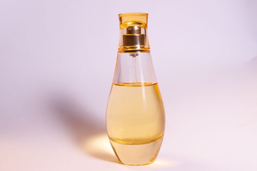 Warm yellow colour glass parfum bottle on white-purple background.