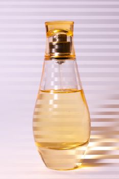 Warm yellow colour glass parfum bottle on white-purple background. Photo contains stripes.