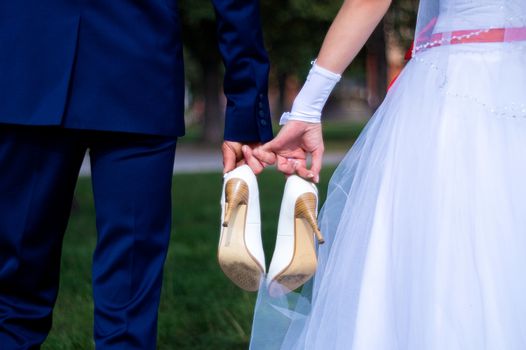 The bride and groom hold the shoes of the bride between themselves and hold hands with their little fingers. Wedding in detail.