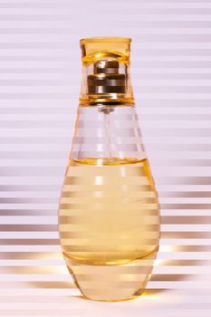 Warm yellow colour glass parfum bottle on white-purple background. Photo contains stripes.