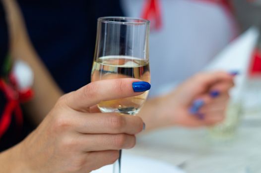 Guest holds glass with bubbly champagne in weddind. Wedding details in close-up view.