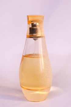 Warm yellow colour glass parfum bottle with artificial snow on white-purple background. Closeup view.