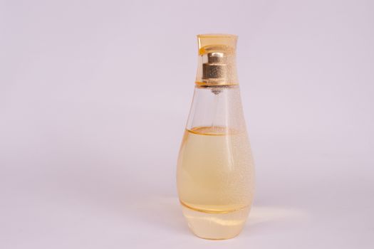 Warm yellow colour glass parfum bottle with artificial snow on white-purple background. Closeup view.