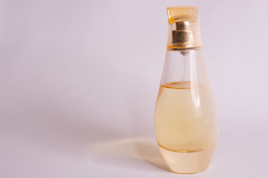 Warm yellow colour glass parfum bottle with artificial snow on white-purple background. Closeup view.