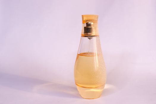 Warm yellow colour glass parfum bottle with artificial snow on white-purple background. Closeup view.