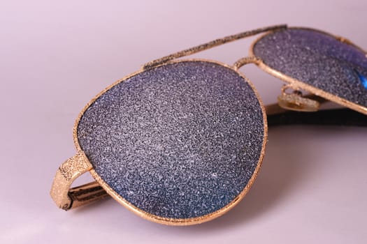 Sunglasses with artificial snow on white-purple background close-up view.