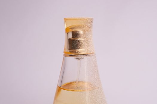 Warm yellow colour glass parfum bottle with artificial snow on white-purple background. Closeup view.