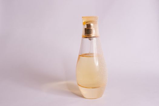 Warm yellow colour glass parfum bottle with artificial snow on white-purple background. Closeup view.