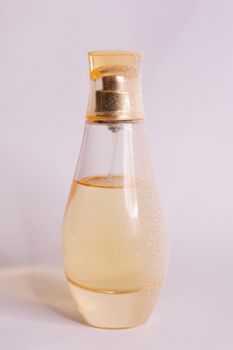 Warm yellow colour glass parfum bottle with artificial snow on white-purple background. Closeup view.