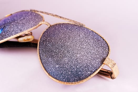 Sunglasses with artificial snow on white-purple background close-up view.