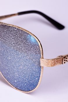 Sunglasses with artificial snow on white-purple background close-up view.