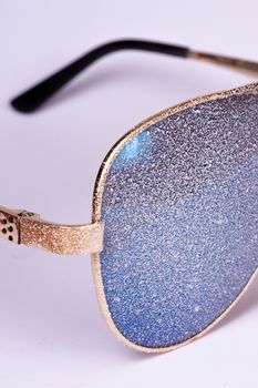 Sunglasses with artificial snow on white-purple background close-up view.
