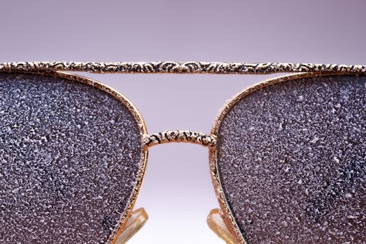 Sunglasses with artificial snow on white-purple background close-up view.