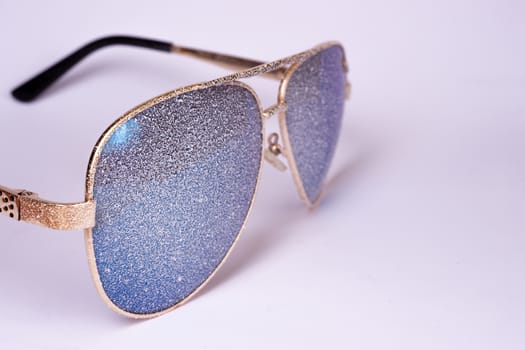 Sunglasses with artificial snow on white-purple background close-up view.