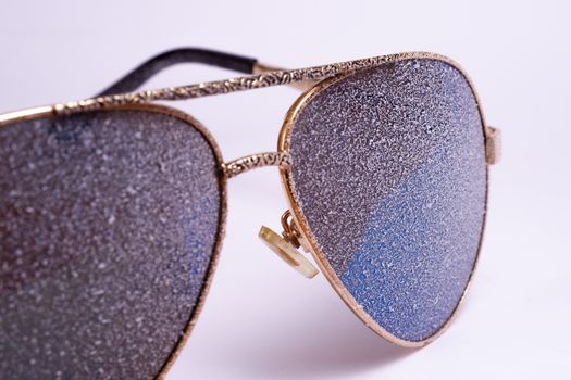 Sunglasses with artificial snow on white-purple background close-up view.