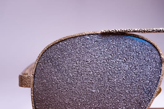 Sunglasses with artificial snow on white-purple background close-up view.