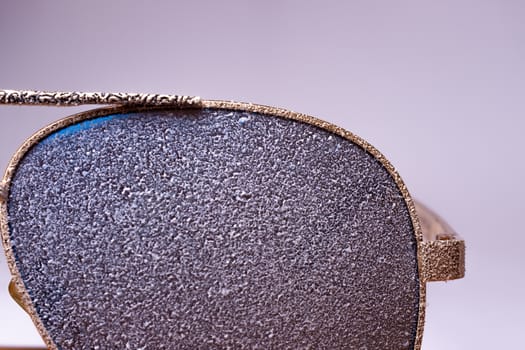 Sunglasses with artificial snow on white-purple background close-up view.