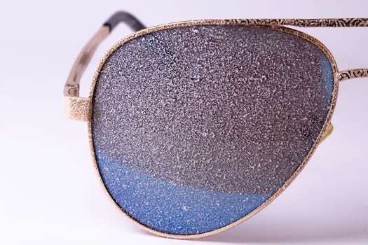 Sunglasses with artificial snow on white-purple background close-up view.