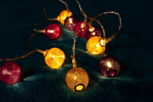 Battery garland with metallic grid balls on blue blanket. Closeup view with blurred background.