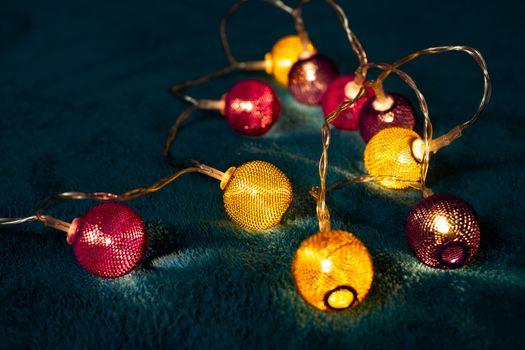 Battery garland with metallic grid balls on blue blanket. Closeup view with blurred background.