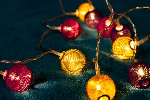 Battery garland with metallic grid balls on blue blanket. Closeup view with blurred background.